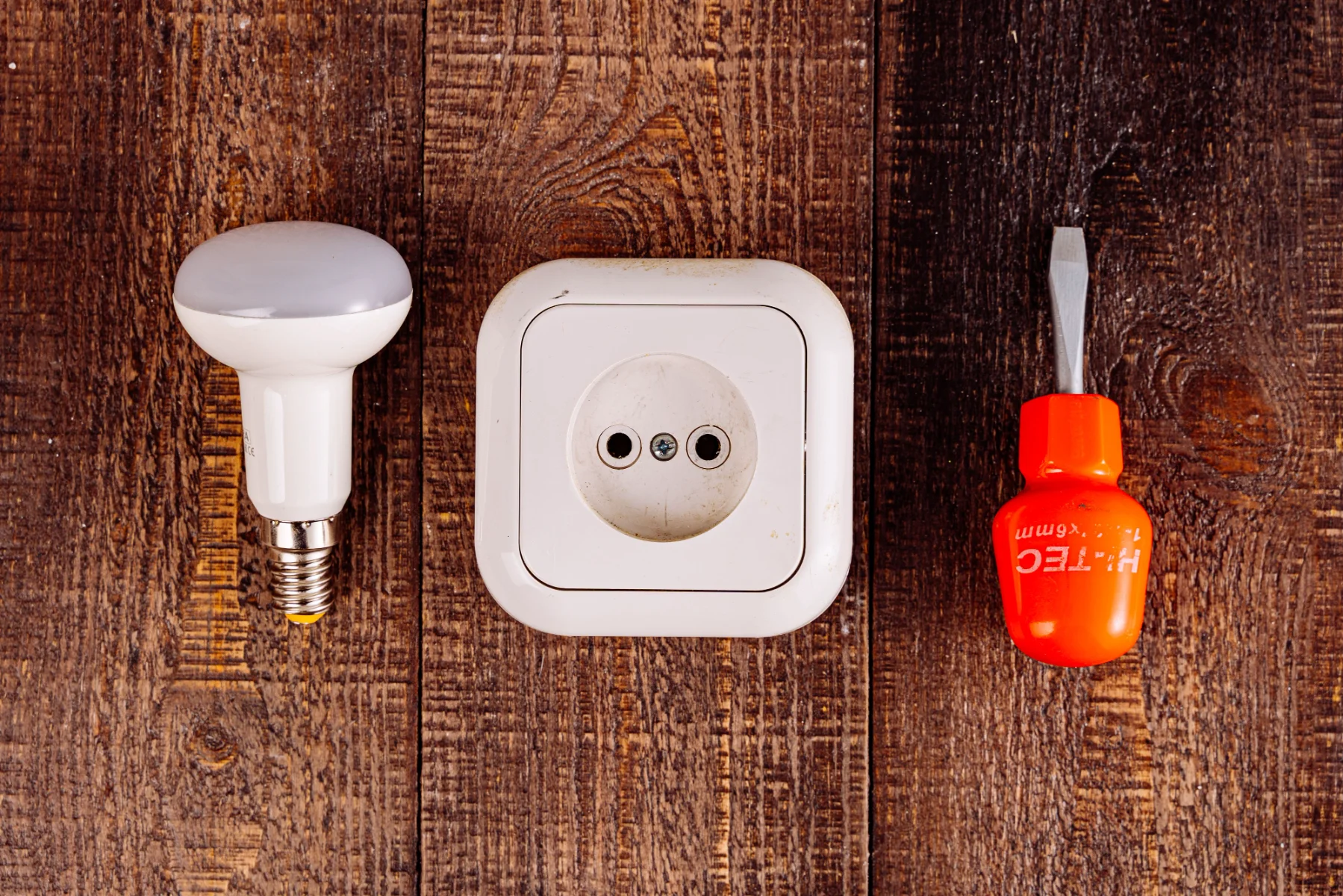 Żarówka LED, gniazdo elektryczne i śrubokręt na drewnianym blacie